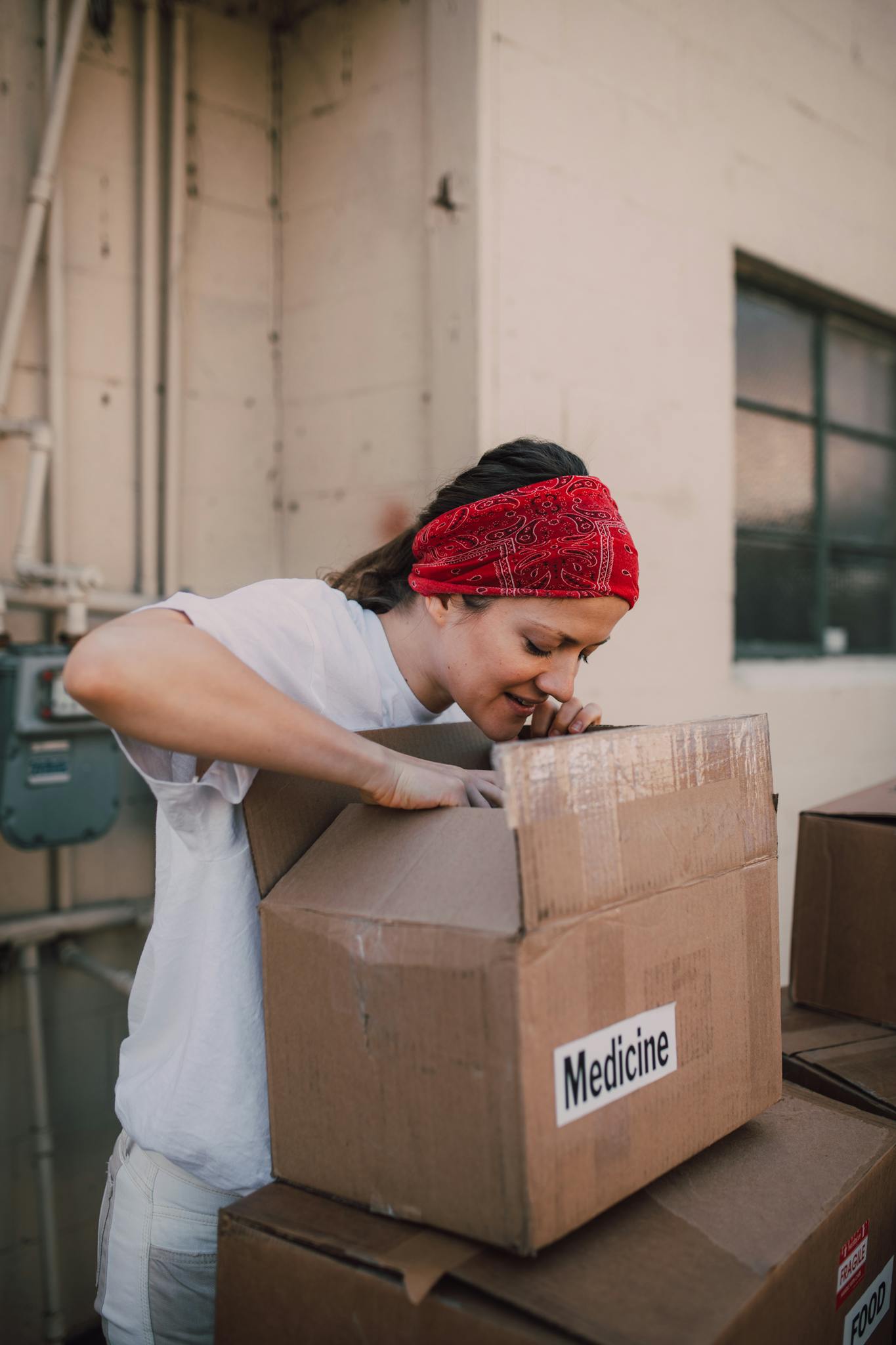 A volunteer adult woman opens a medicine box outdoors, engaging in community service.
