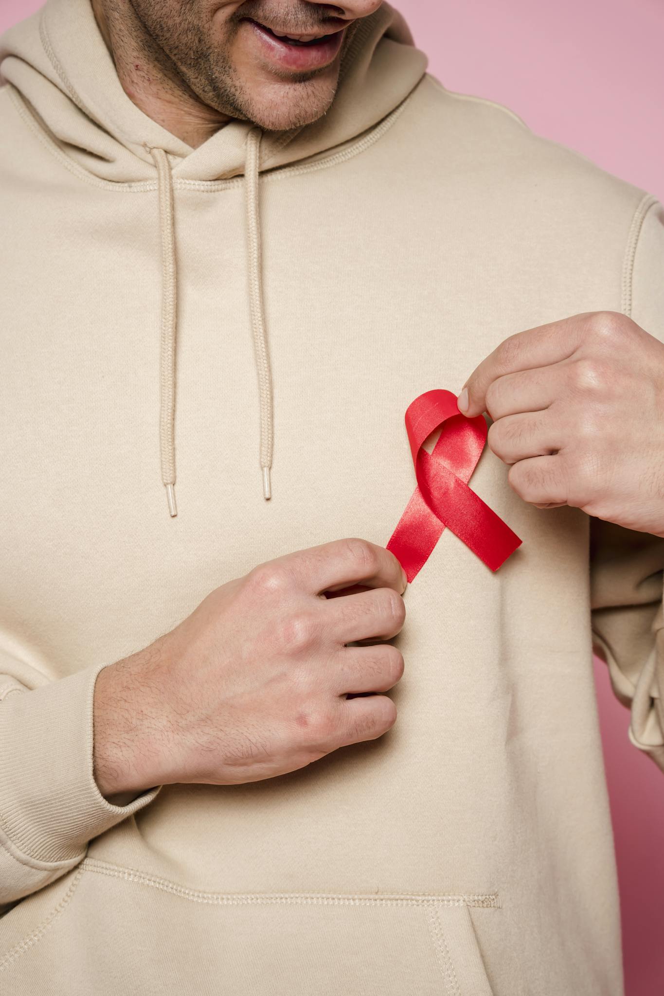 Man in hoodie holding red ribbon symbolizing awareness and support.